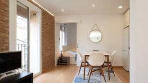 Una sala moderna con televisor, un comedor con mesa y sillas, un espejo, y una puerta que da a otra habitación.
