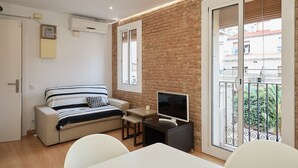 Un espacio habitable pequeño con sofá, televisor y balcón con barandilla de metal.