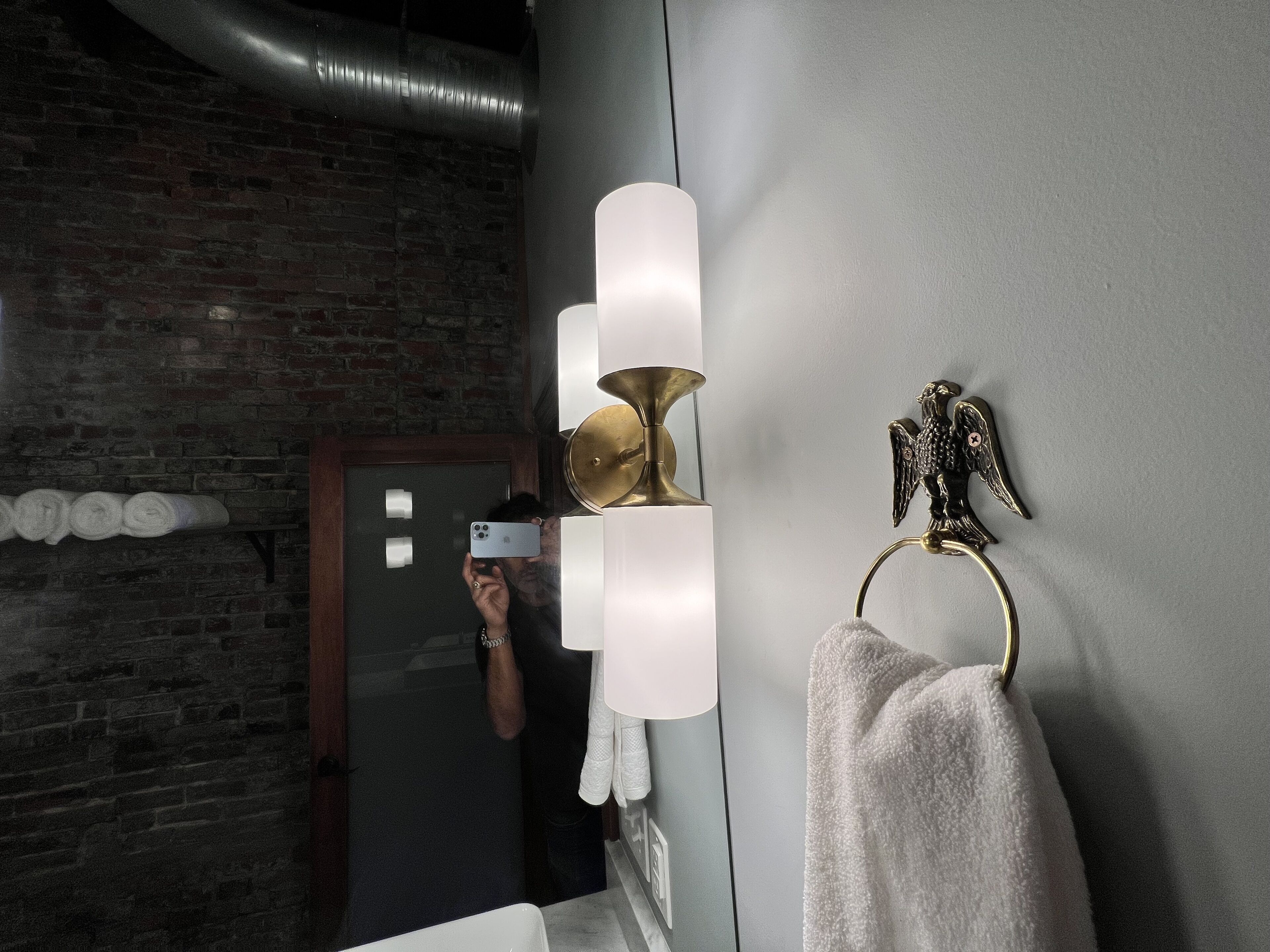 A bathroom with a brick wall, a towel rack with a towel, a mirror, and a wall-mounted light fixture.