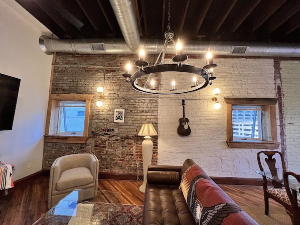 Un salon chaleureux avec un mur en briques, un lustre, une guitare et un canapé.