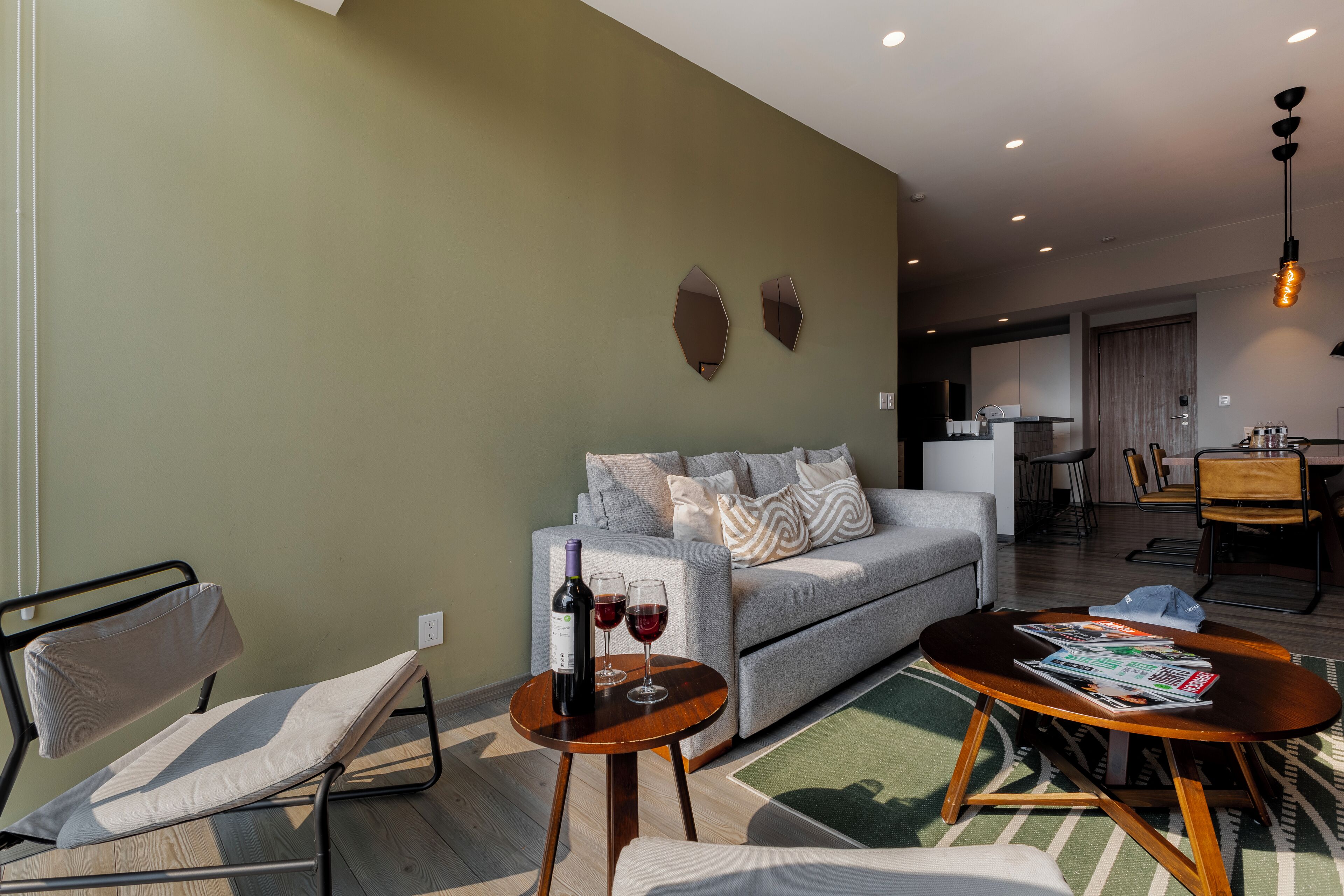 A modern living room with a sofa, a coffee table, and a chair. There is a bottle of wine and two glasses on the coffee table.