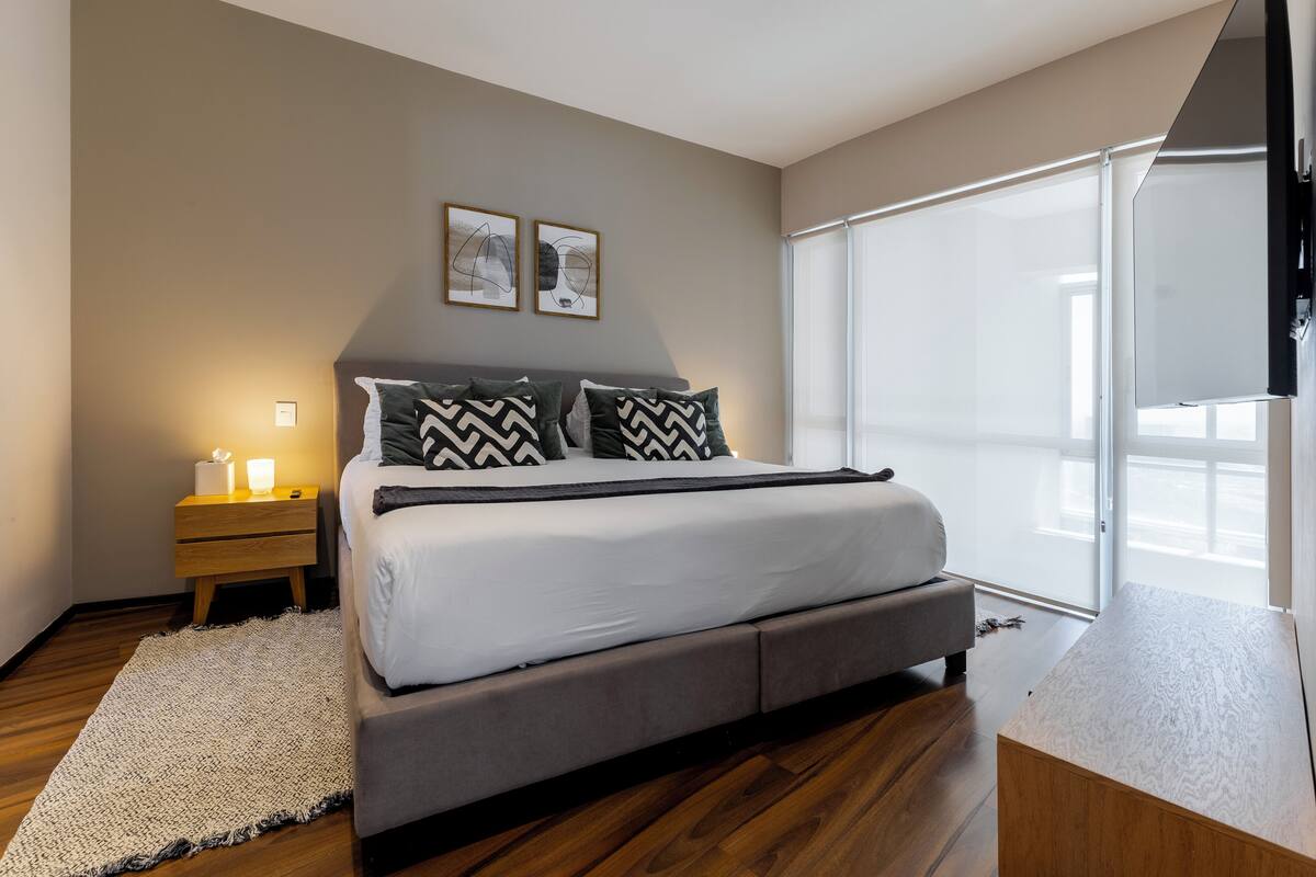 A modern bedroom with a large bed, a nightstand, and a window with blinds.