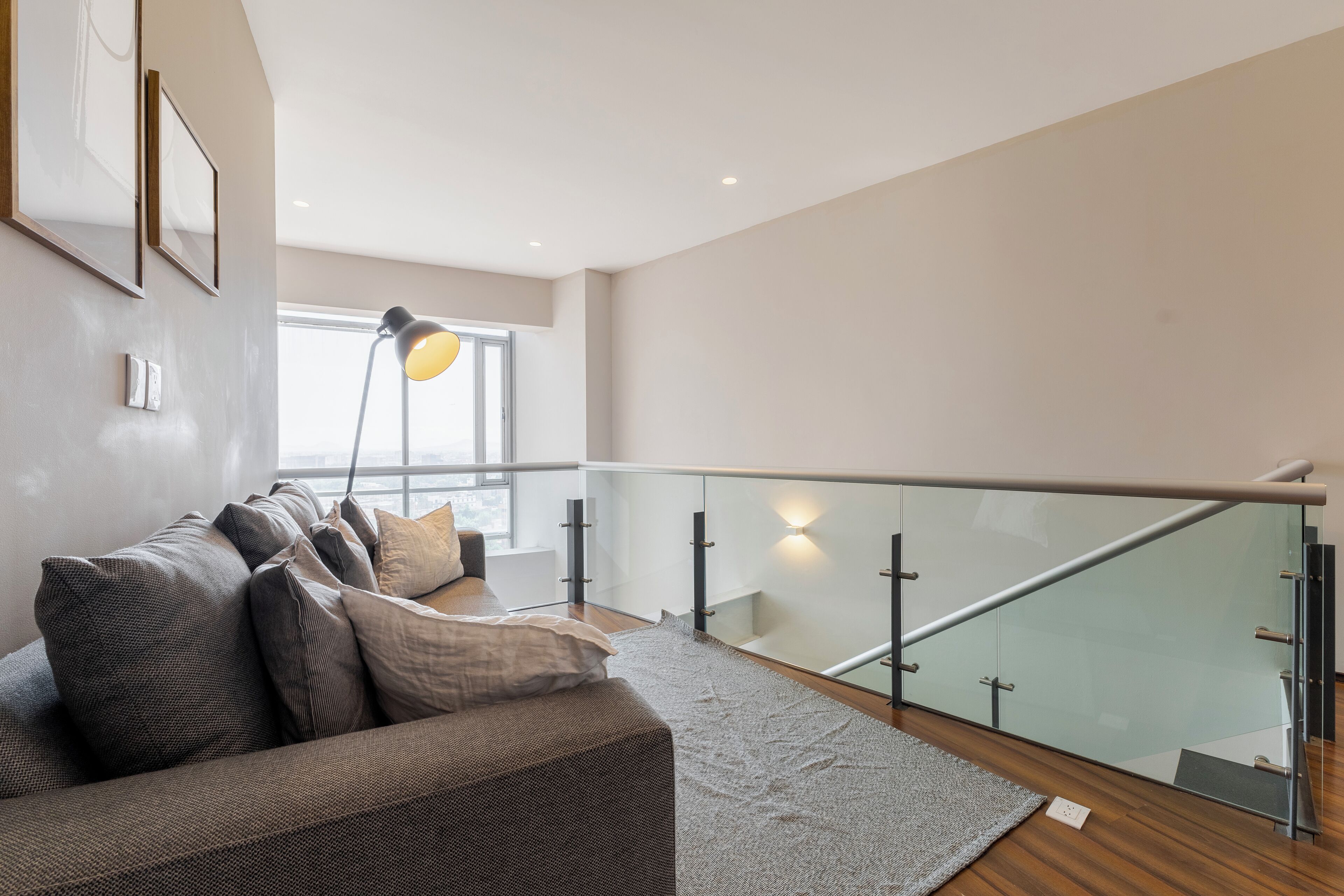 A modern living room with a sofa, a glass railing, and a lamp.