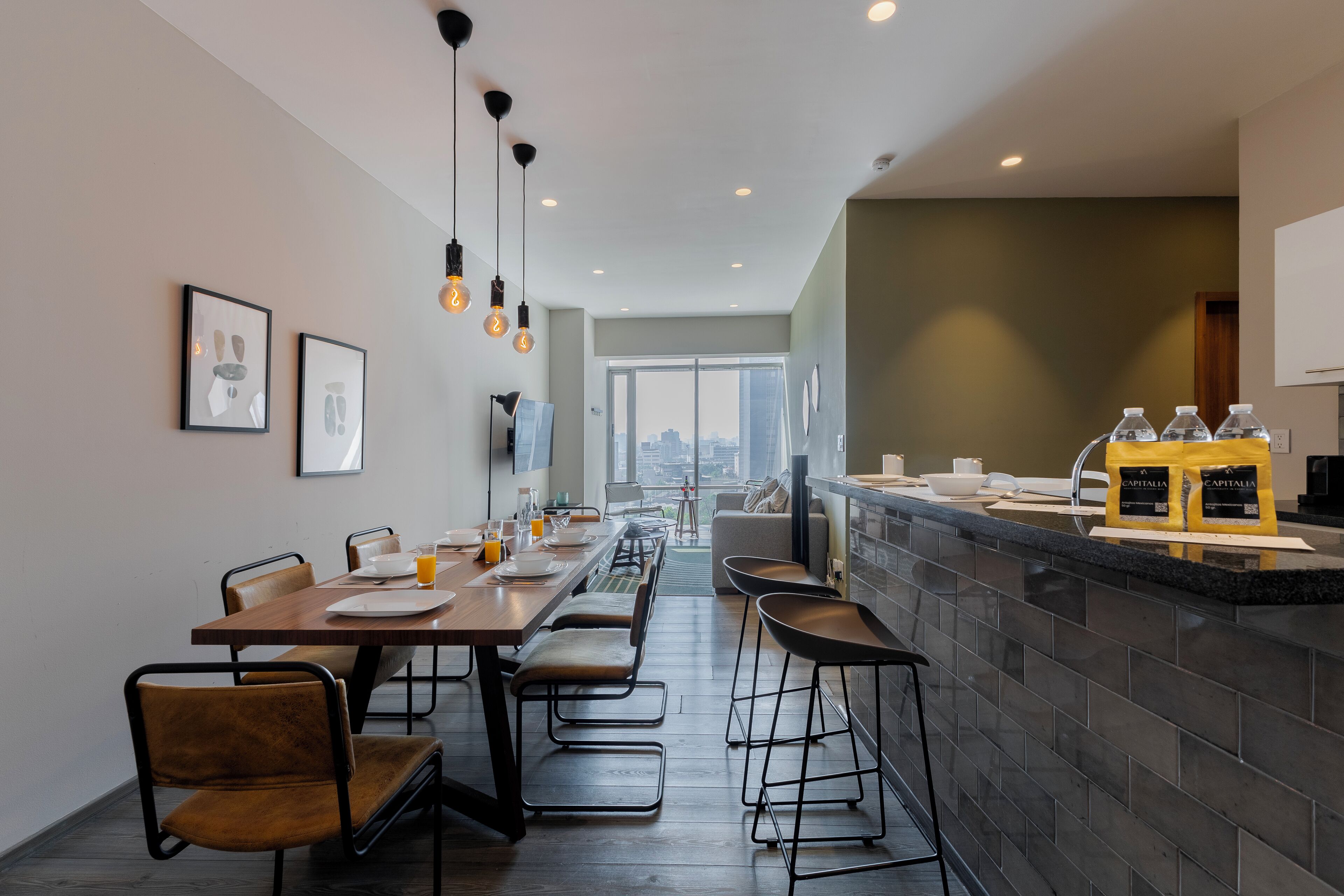 A modern dining area with a long table, bar stools, and a kitchen counter with coffee bags.