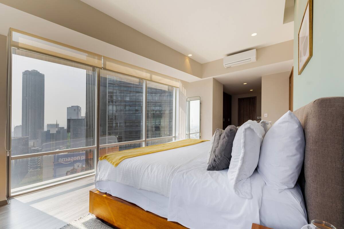 A modern hotel room with a large bed, a view of the cityscape, and a large window.