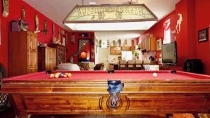 Une table de billard dans une pièce aux murs rouges, avec des meubles en bois et un téléviseur.