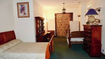 A room with a bed, a wooden dresser, a chair, a desk, and a lamp.