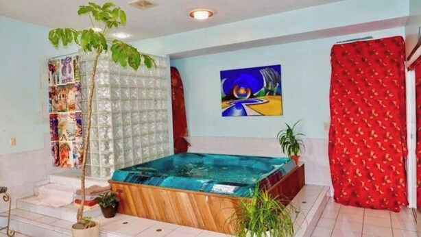 Une salle de spa dotée d’un bain à remous en bois, d’une paroi en verre et d’un tableau au mur.