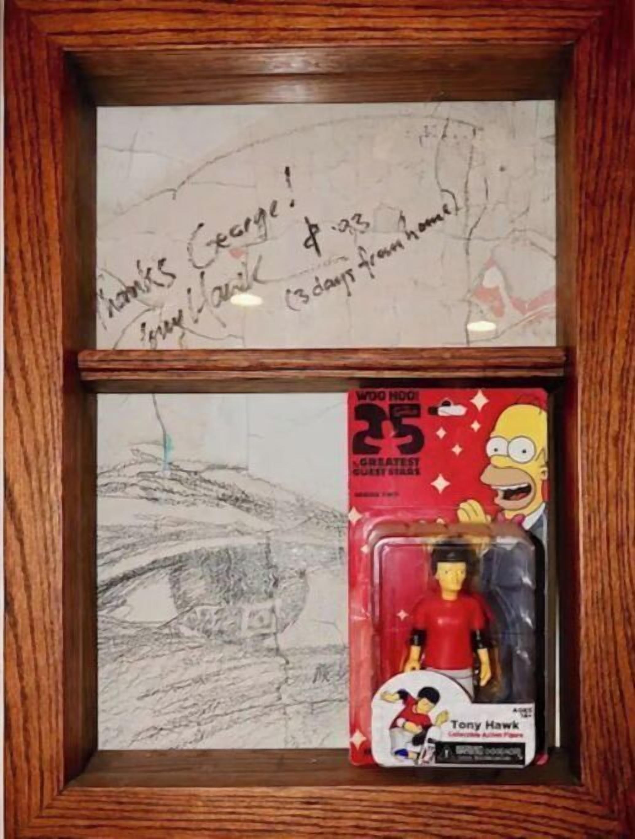 Ein gerahmtes Kunstwerk mit einer signierten Notiz und einer Spielzeugfigur in einer Schachtel.
