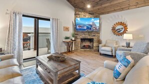 A cozy living room with a stone fireplace, comfortable seating, and a large TV. - Luxury Lodge w/ Hot Tub + Boat Slip | 2 Min to Silver Dollar City! (Branson)