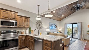 A kitchen with wooden cabinets, stainless steel appliances, a granite countertop, and a dining area with a sofa and table. - Luxury Lodge w/ Hot Tub + Boat Slip | 2 Min to Silver Dollar City! (Branson)