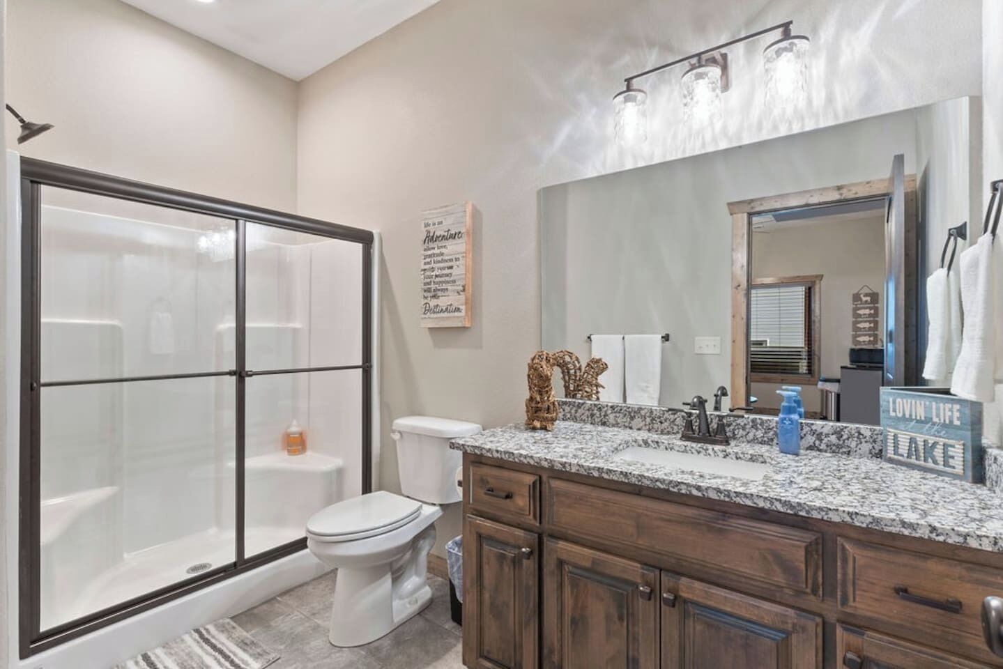 A bathroom with a glass shower enclosure, a toilet, a vanity with a mirror, and a sign that reads "Lovin' Life at the Lake".