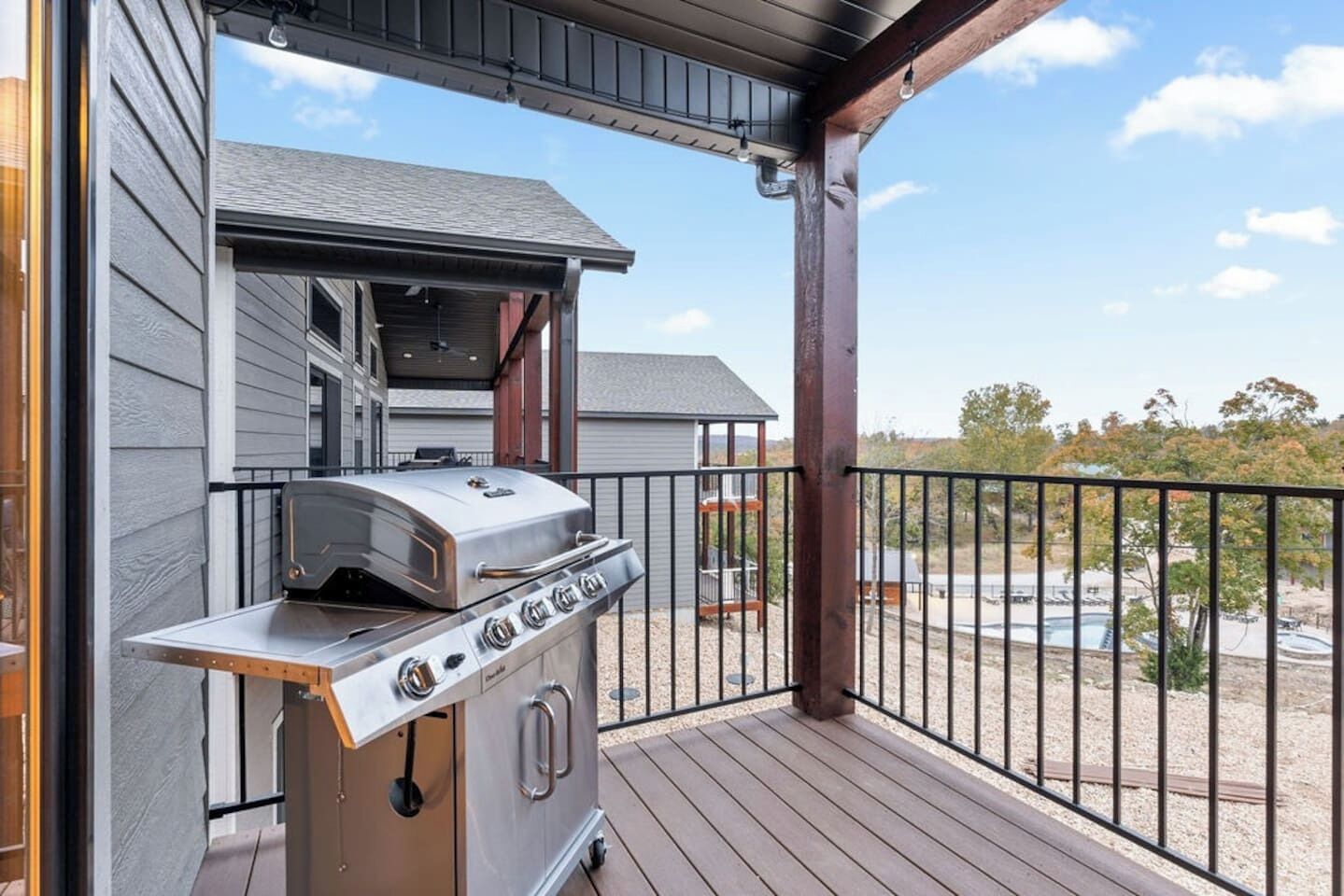 Ein Grill mit Holzbalkon und Blick auf Pool und Bäume.