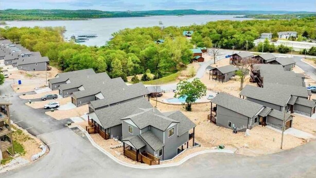 A residential area with multiple houses, a road, and a body of water in the background. - Luxury Lodge w/ Hot Tub + Boat Slip | 2 Min to Silver Dollar City! (Branson)