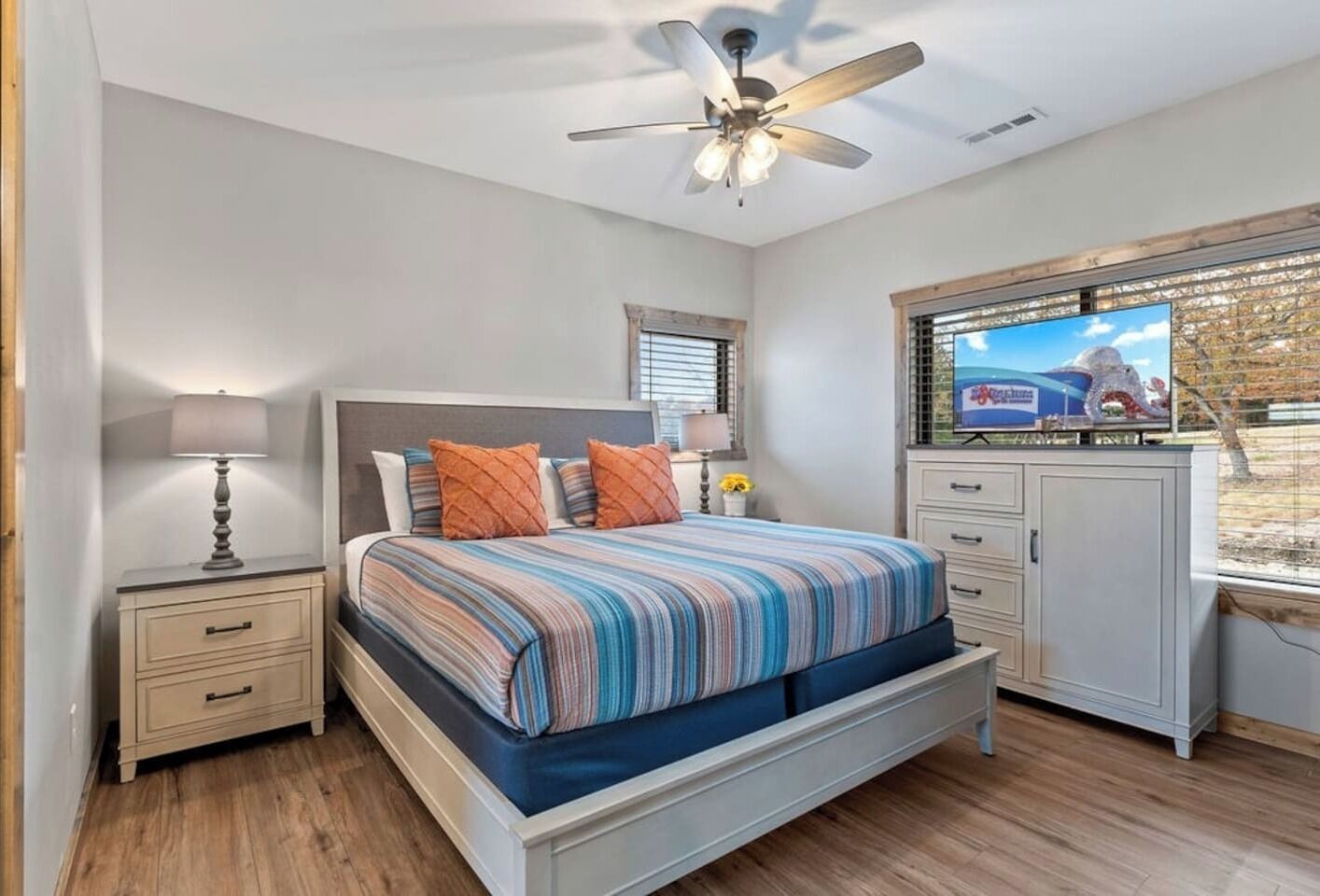 A bedroom with a bed, nightstands, a ceiling fan, a TV, and a window with blinds.