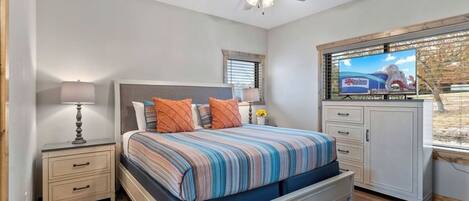 A bedroom with a bed, nightstands, a ceiling fan, a TV, and a window with blinds.