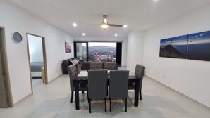 Ein moderner Essbereich mit großem Tisch und Stühlen, einem Deckenventilator und Blick auf die Stadt durch große Fenster.