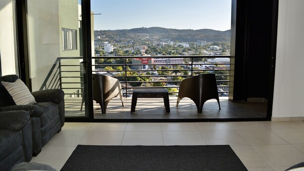 Ein Wohnzimmer mit einer Couch, zwei Korbstühlen, einem kleinen Tisch und Blick auf eine Stadtlandschaft durch eine Schiebetür.