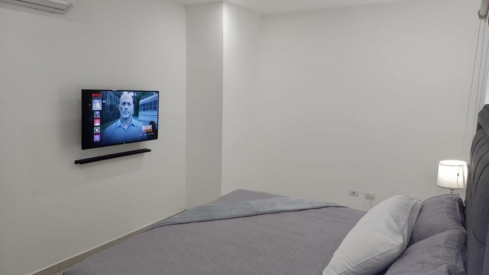 Une chambre à coucher avec un lit, un téléviseur fixé au mur et une lampe de chevet.