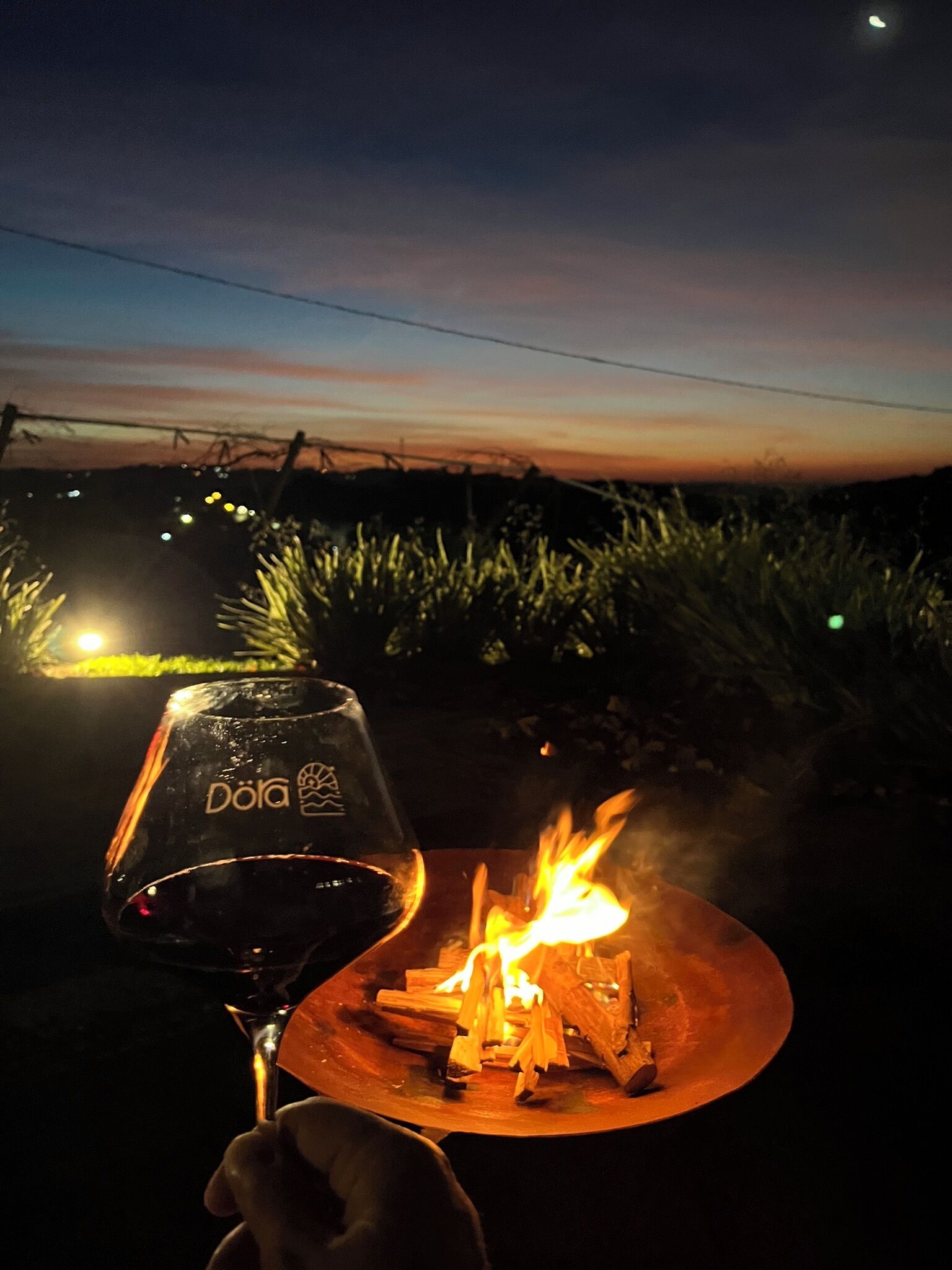 Un verre orné d’un logo, un feu sur une table et un ciel nocturne.