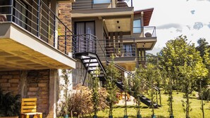Un immeuble moderne à plusieurs étages, doté de balcons, d’une façade en pierre et d’un jardin bien entretenu.