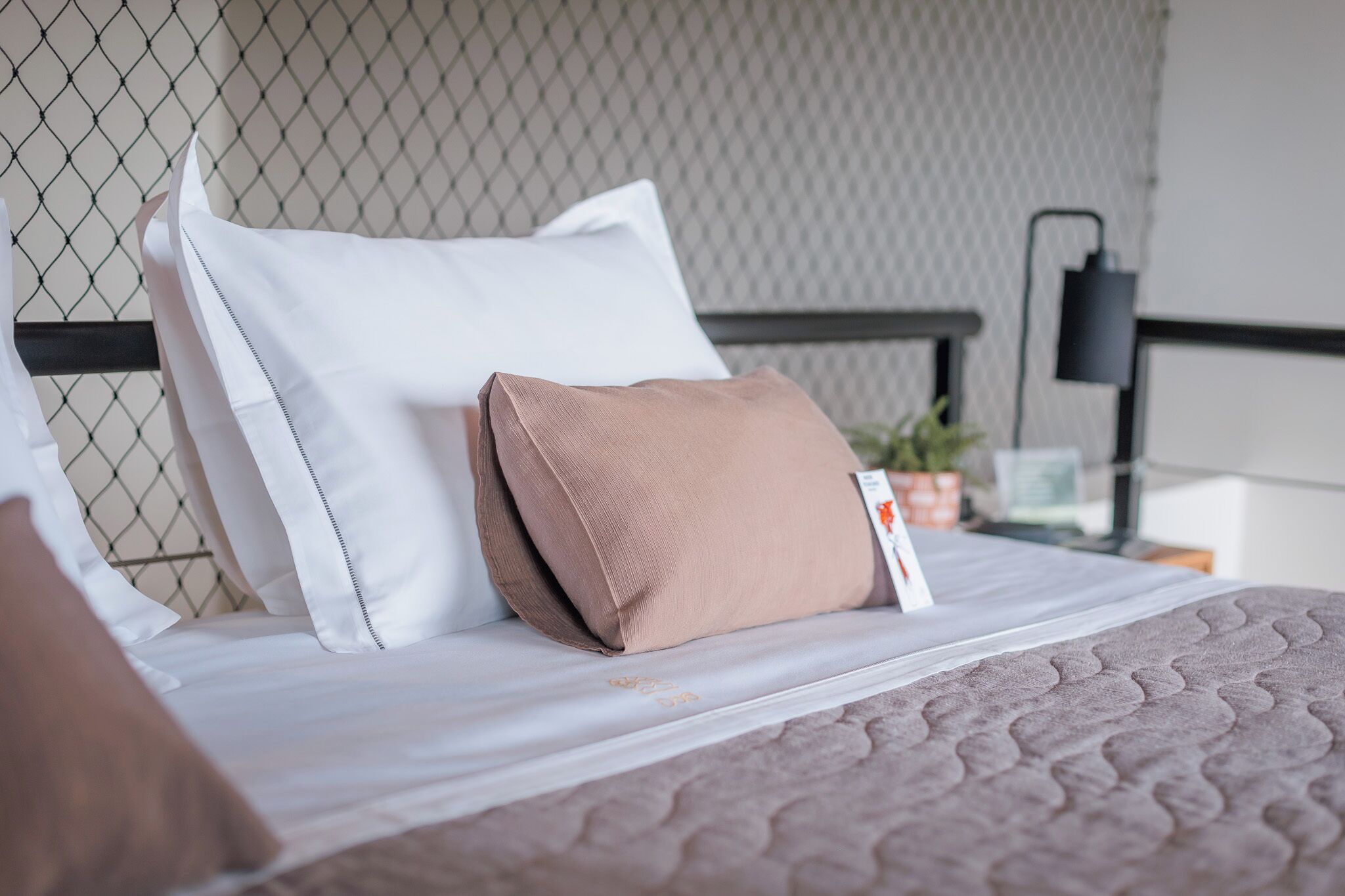 A neatly made bed with white and brown pillows, a quilted blanket, and a headboard against a textured wall.