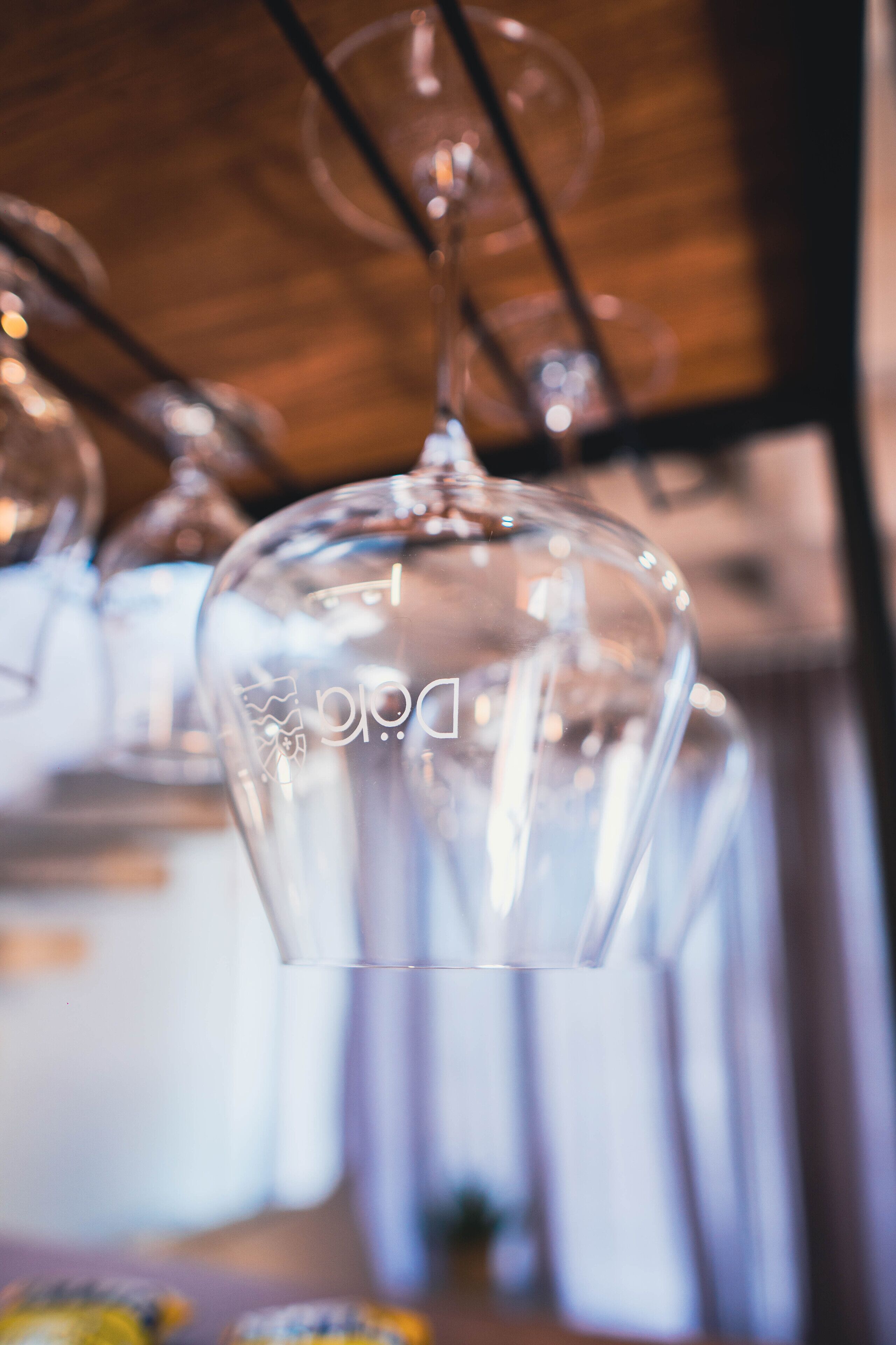 A clear glass wine glass with a logo, hanging from a metal rack.