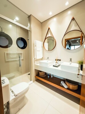 Une salle de bain moderne avec une douche à l’italienne en verre, des toilettes blanches, un meuble-lavabo double avec un miroir et une étagère en bois.