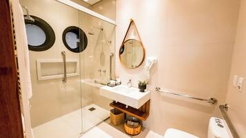 Un baño moderno con ducha de vidrio, un lavamanos blanco con un espejo encima y un inodoro con barra de apoyo.