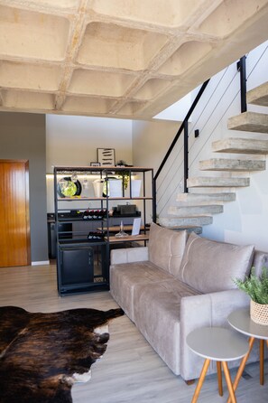 Un salon moderne comprenant un canapé, une table basse, un tapis, un escalier et une étagère décorative.