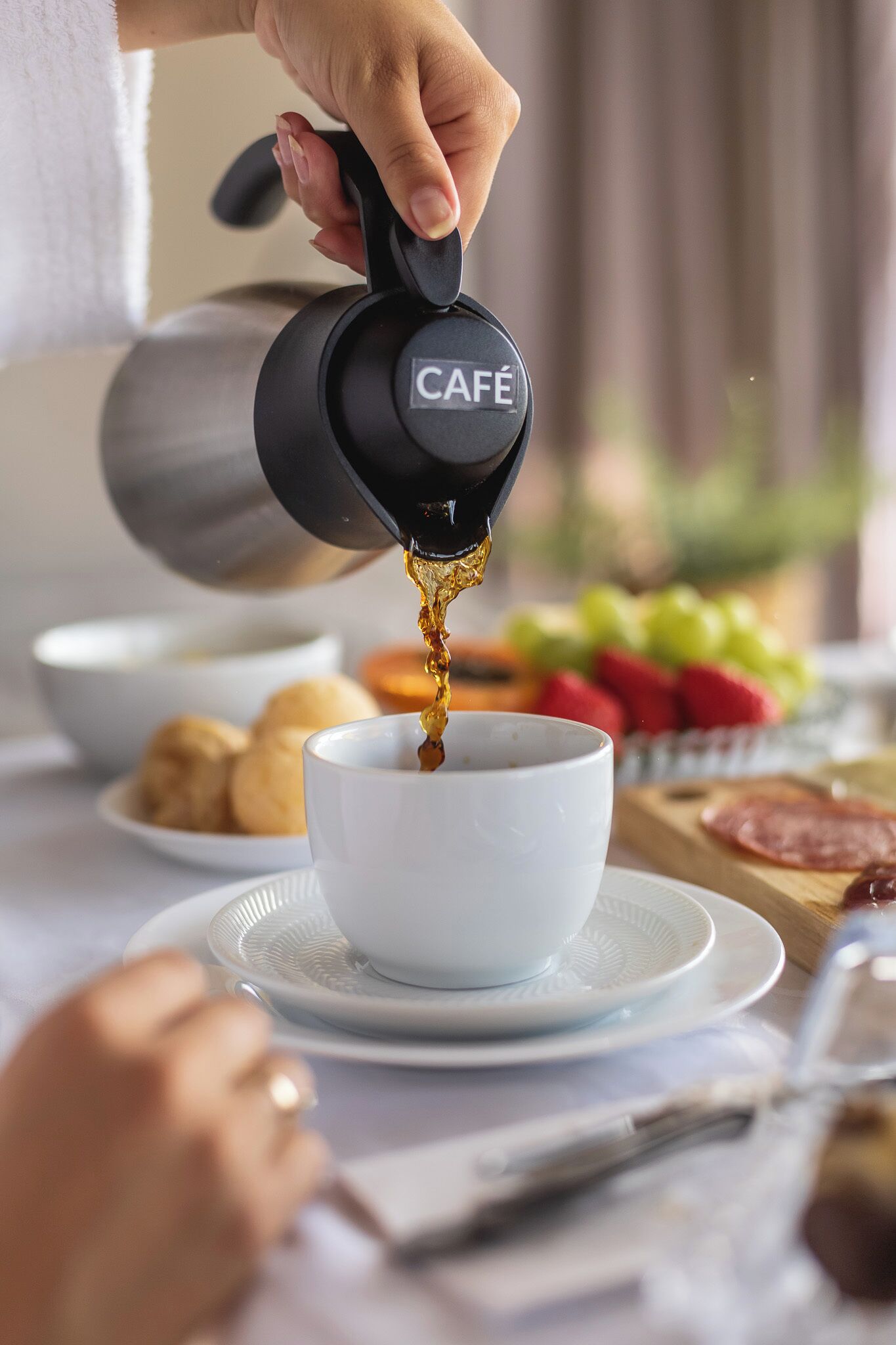 A hand pouring coffee from a branded coffee maker into a cup.