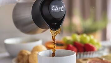 A hand pouring coffee from a branded coffee maker into a cup.