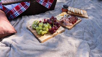 A picnic setup with a blanket, a basket, and a wooden board with grapes, cheese, and meats.