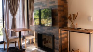 Un salon moderne doté d’une cheminée, d’un téléviseur, d’un coin repas avec des chaises et d’une grande fenêtre avec des rideaux.
