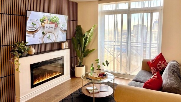 A living room with a fireplace, a television, a sofa, and a large window with a city view. - Spacious 3 Bedroom 2 Bath Condo in Toronto (Toronto)