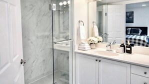 A modern bathroom with a glass shower enclosure, a vanity with a sink, and a large mirror with lights above. - Spacious 3 Bedroom 2 Bath Condo in Toronto (Toronto)