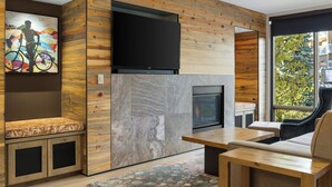 A modern living room with a fireplace, wooden panel walls, a mounted TV, and a seating area with a view of the outdoors. - Club Wyndham Resort at Avon (Avon)