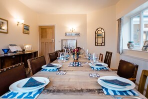Ein Esszimmer mit einem langen Tisch, gedeckt für eine Mahlzeit, mit blau-weißem Geschirr und Stühlen.