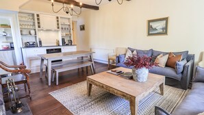 A cozy living room with a wooden coffee table, a grey sofa, and a dining area with a bench and white cabinets.