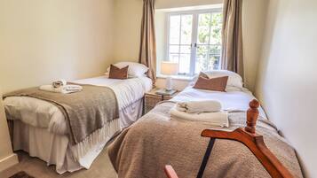 Un dormitorio doble con dos camas, una ventana con cortinas, una mesita de noche con lámpara y una silla de madera.