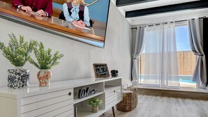 Ett modernt vardagsrum med ett vitt konsolbord, en väggmonterad TV och utsikt över en pool genom stora fönster.