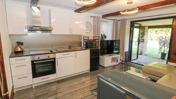 A modern kitchen with stainless steel appliances, a built-in oven, a microwave, and a television. There is a dining area with a table and chairs, and a view of a garden through a glass door.