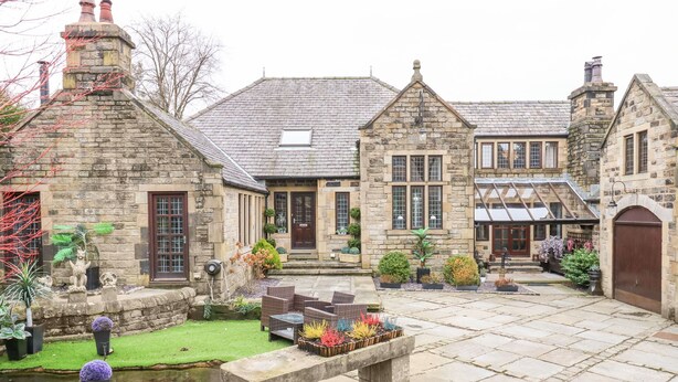 A stone building with a courtyard, featuring a stone bench, a small pond, and various potted plants. - Moor Cottage (Oldham)