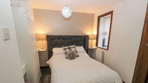 A bedroom with a large bed, a headboard, bedside lamps, a mirror, and a ceiling light fixture. - Moor Cottage (Oldham)