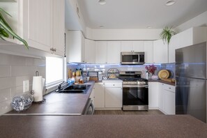 A modern kitchen with white cabinets, stainless steel appliances, and a granite countertop. - Caribe | Luxury King bed, Game-room with Balcony rooftop stay (Atlantic City)