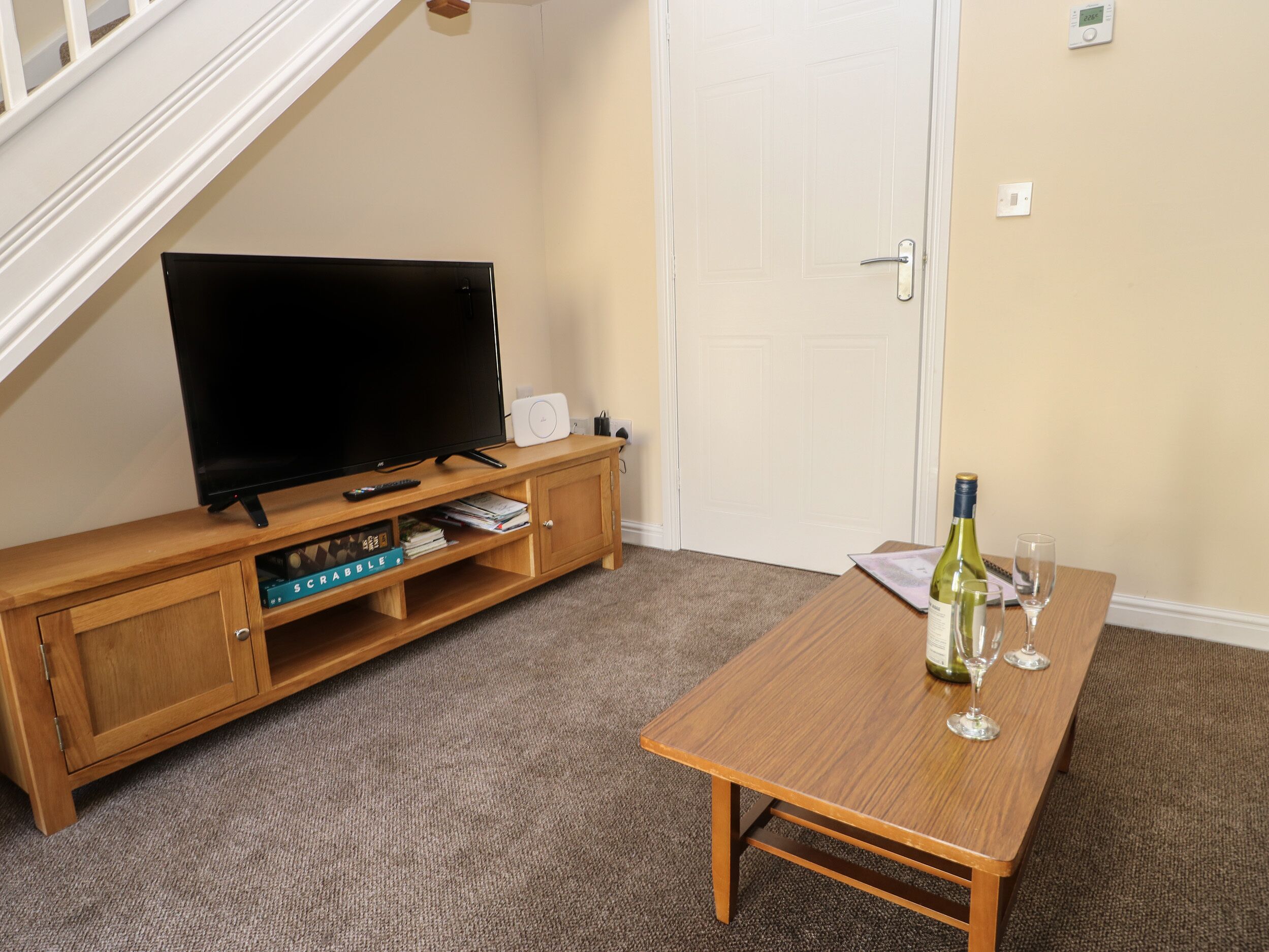 A living room with a TV on a wooden stand, a table with wine glasses, and a door in the background.