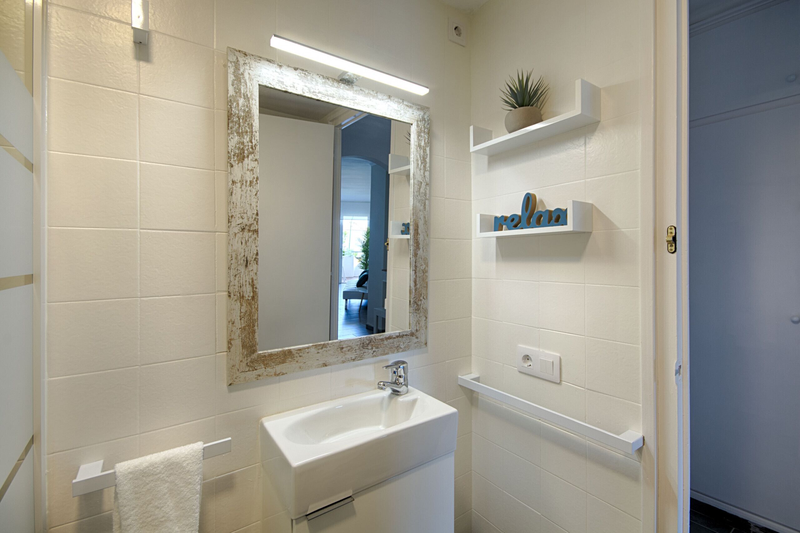 A bathroom with a white sink, a mirror with a distressed frame, and a shelf with toiletries.