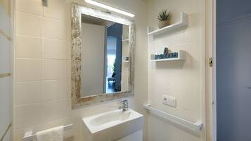 A bathroom with a white sink, a mirror with a distressed frame, and a shelf with toiletries.