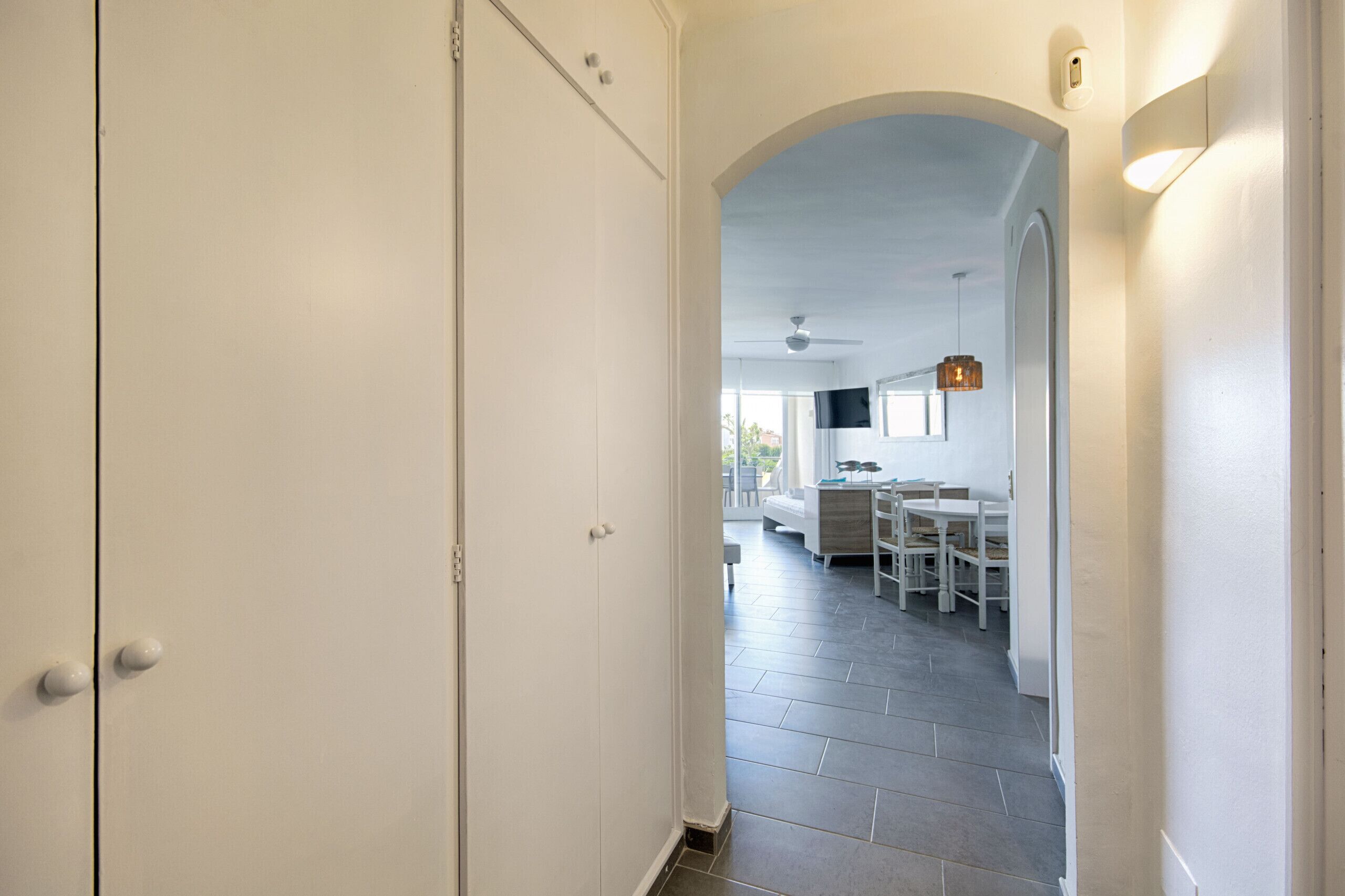 Un pasillo que conduce a un comedor con ventilador de techo, una lámpara colgante y vistas a la cocina.