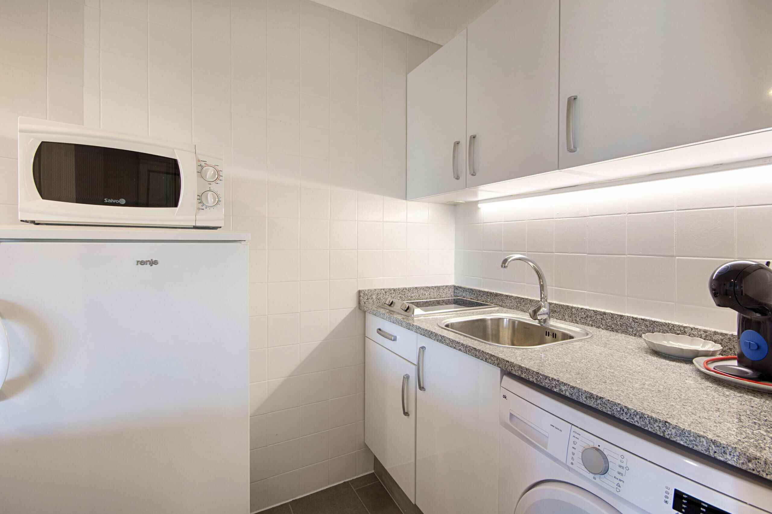 Una cocina compacta con microondas, lavamanos y lavadora.